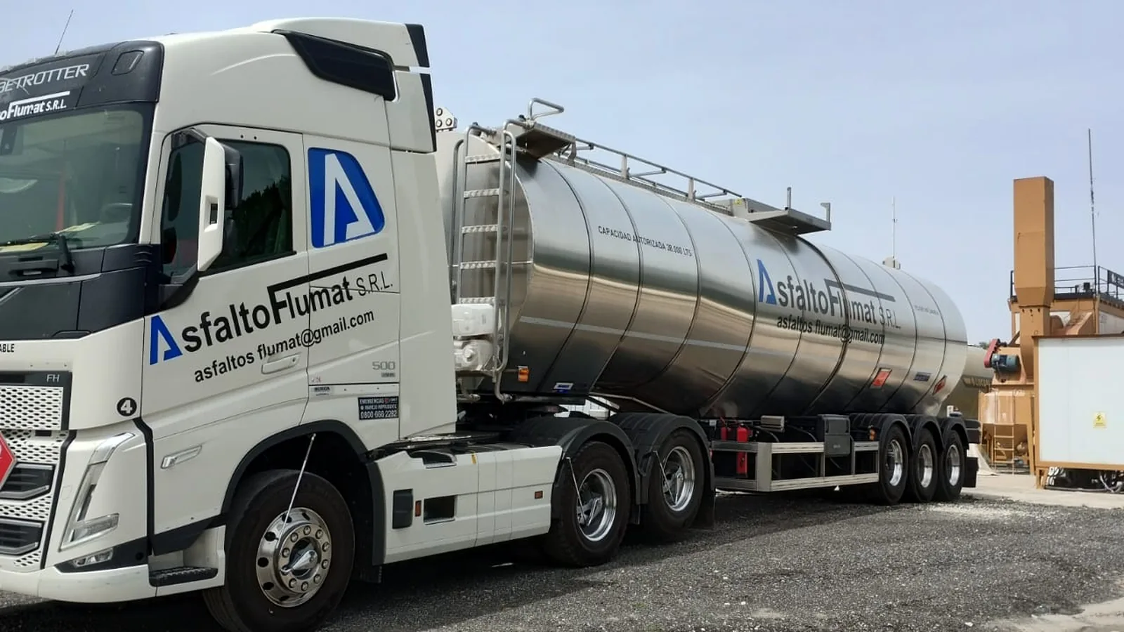 Tractor Volvo FH blanco de Asfalto Flumat con la cisterna cargada, saliendo de la playa de una planta.
