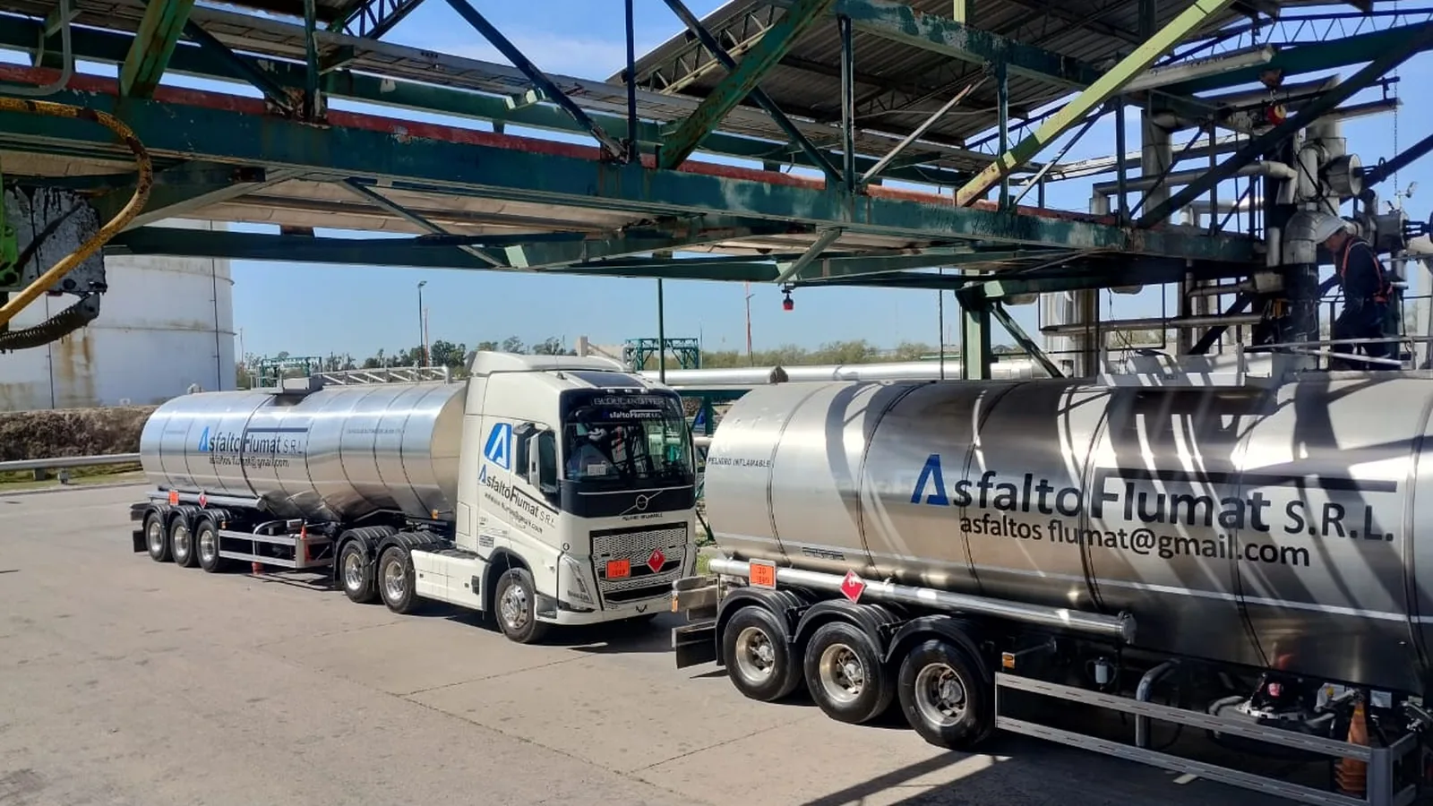 Dos unidades cisterna de Asfalto Flumat cargando en paralelo bajo la estructura metálica del pórtico de una planta.